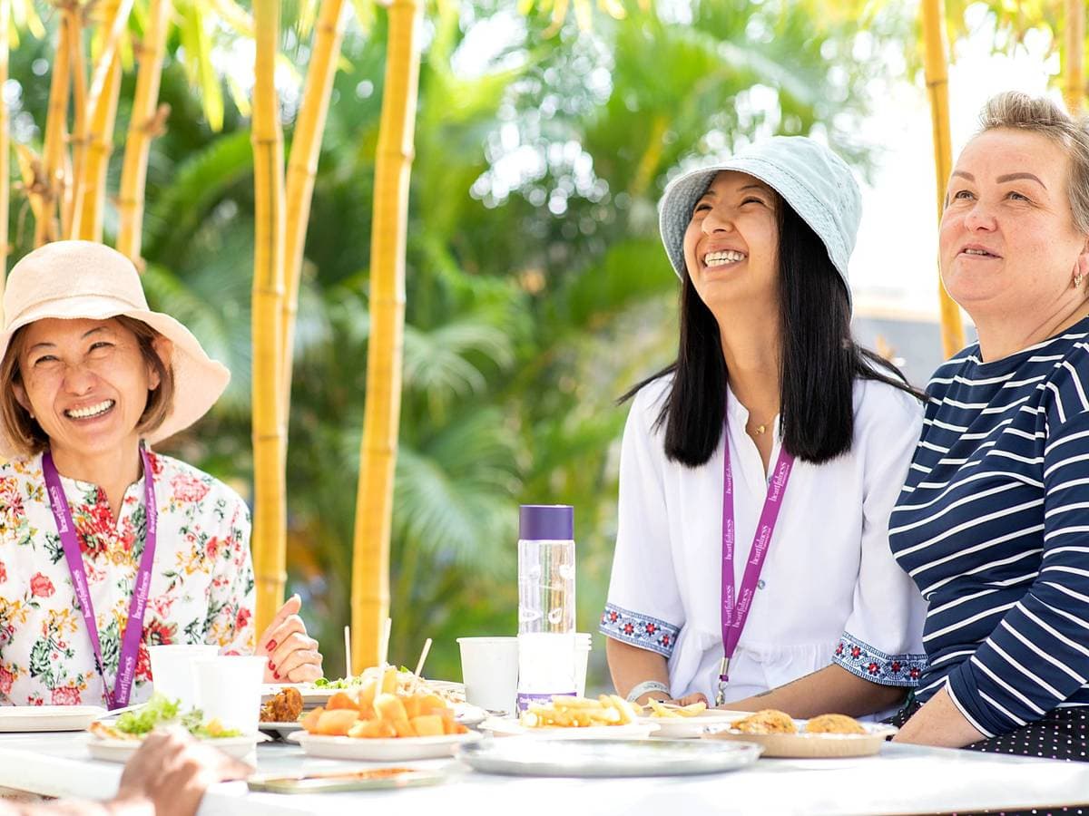Three guests sitting together over lunch at a table outdoors, bamboo behind them.