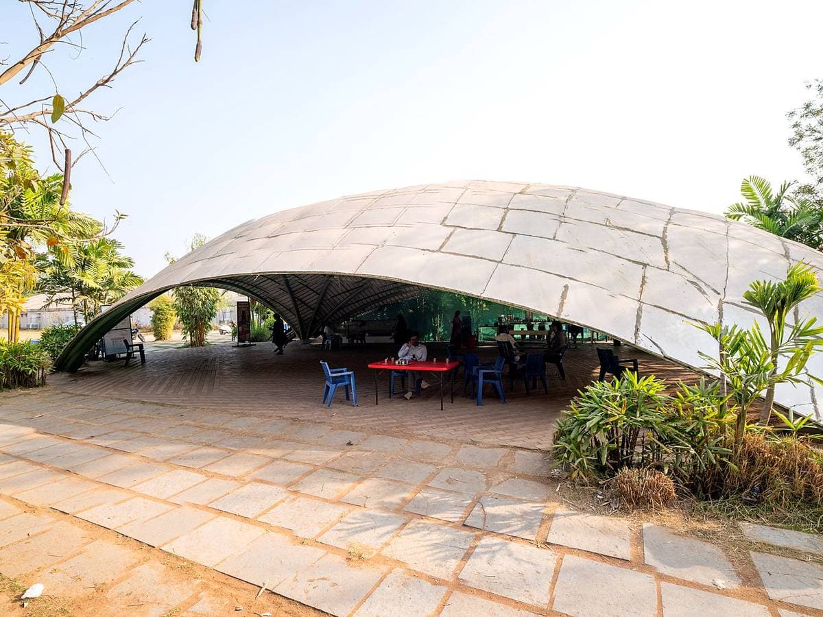 A wide shell canopy over a paved terrace at Kanha, tables set beneath it and planting at the edges.