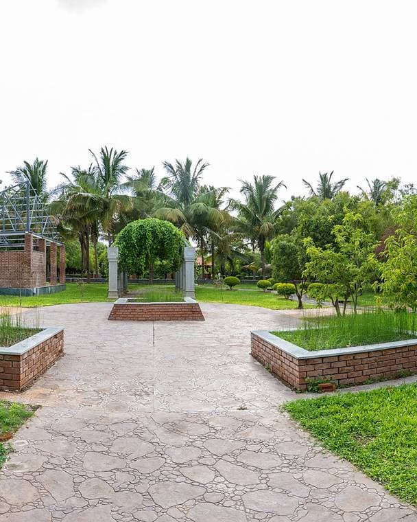 A garden at Babuji Vanam: a circular paved clearing edged with brick, planting beds and young palms around it.