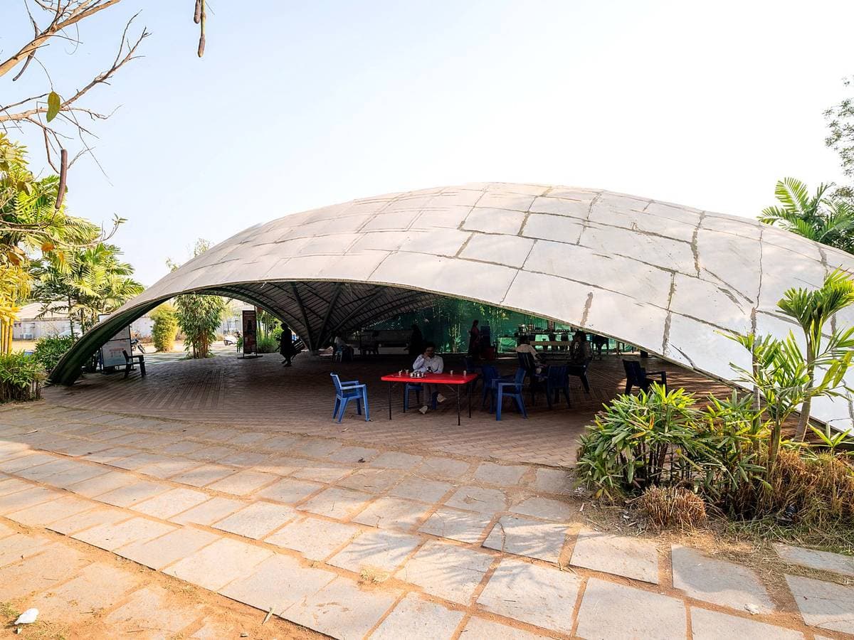A wide shell canopy over a paved terrace at Kanha, tables set out beneath it.