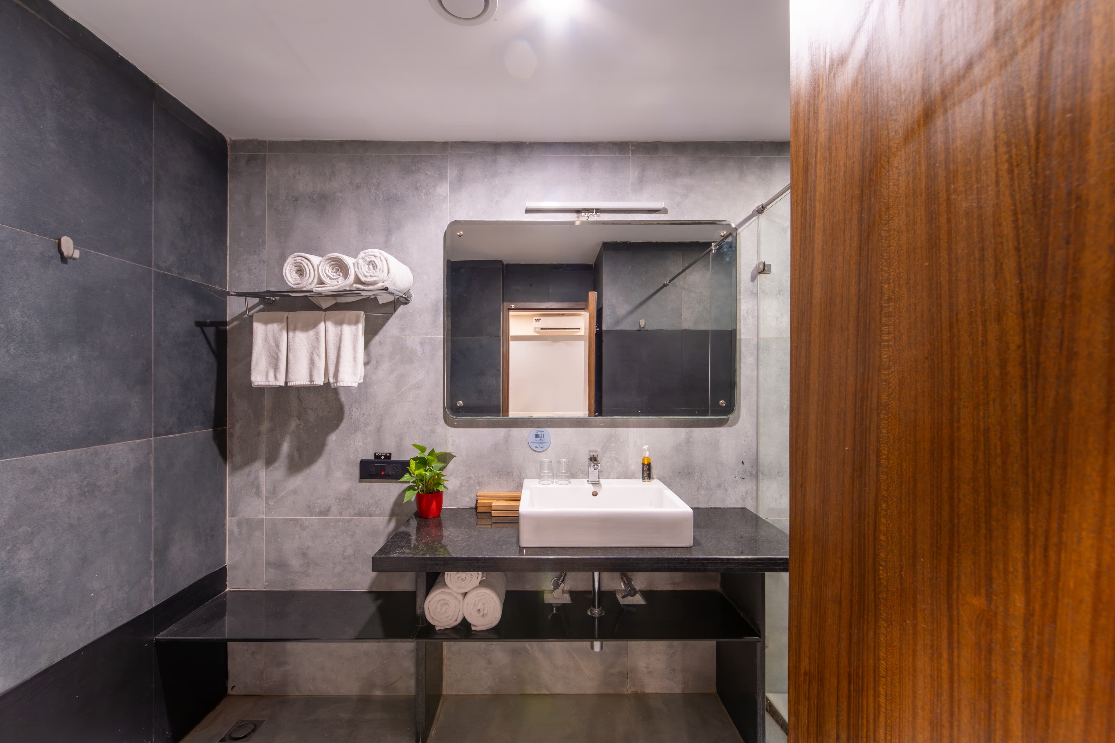 A long wellness bathroom in dark stone, with a twin vanity and walk-in shower.